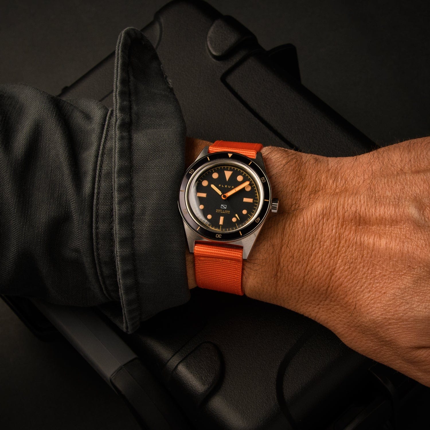 Lifestyle photo of a person wearing a diver watch with an orange nylon NATO strap in a dark setting