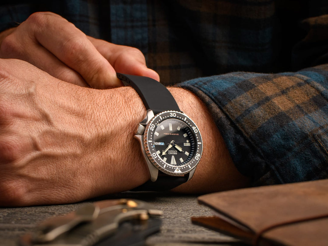 Man wearing a diver-style watch with a black silicone strap featuring a sport clasp