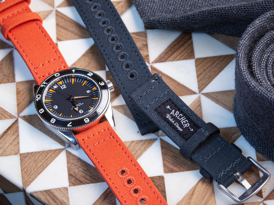Watch with an orange canvas strap next to a navy canvas strap on a patterned surface